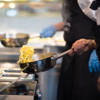 Koch bereitet frische Pasta direkt in der Pfanne zu und schwingt die Pasta aus der Pfanne heraus. 